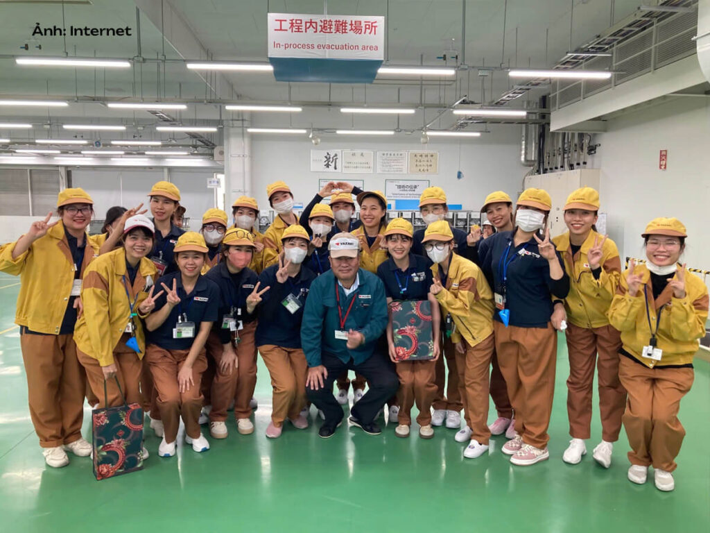 Áo bảo hộ lao động đồng phục công ty Yazaki màu vàng-nâu (Ảnh: Tổng giám đốc Nogi Hiroshi đến thăm các nhân viên EV đang thực tập tại xưởng Makinohara)